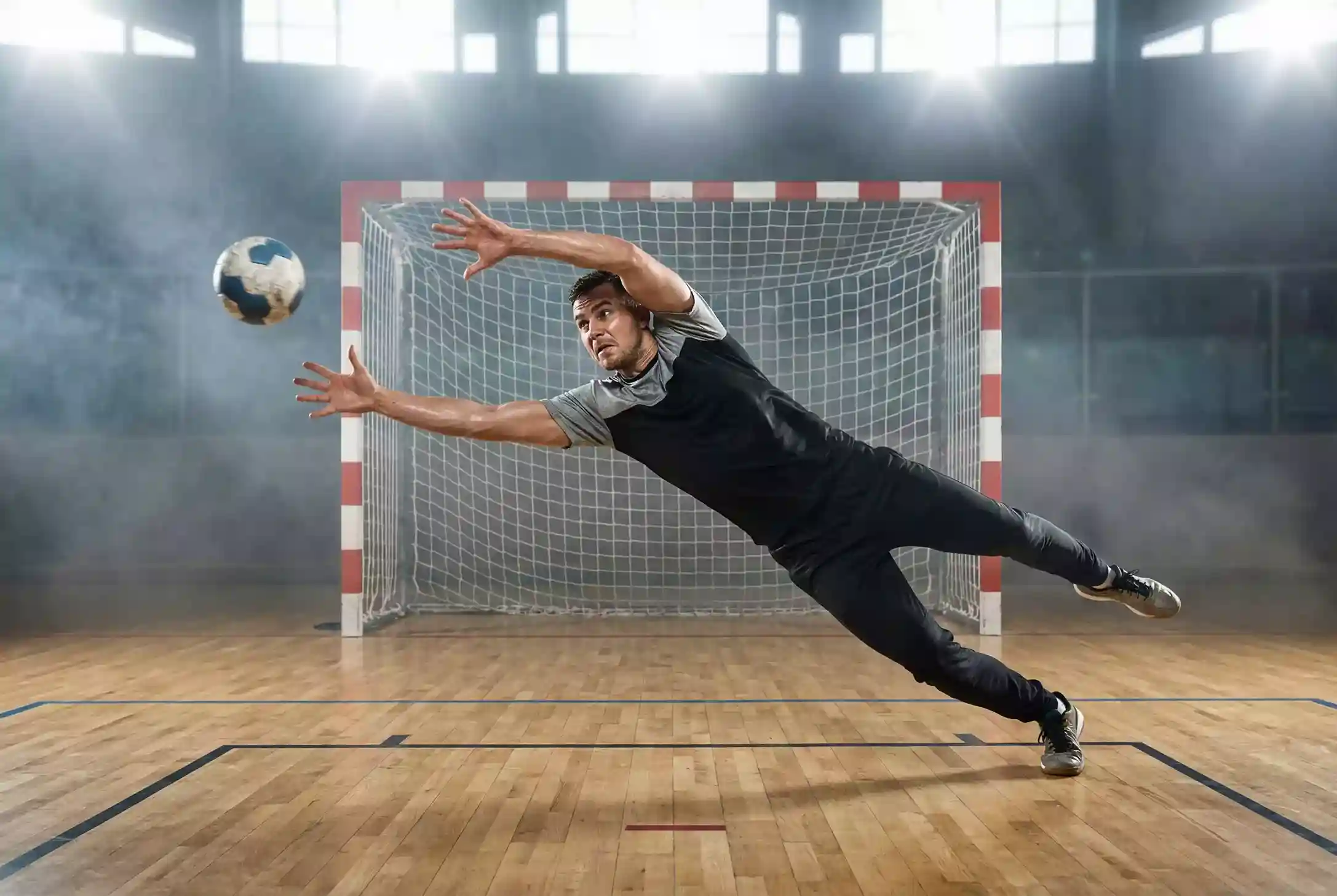 Handball-Torwart hält einen Ball in der Halle bei dramatischem Licht