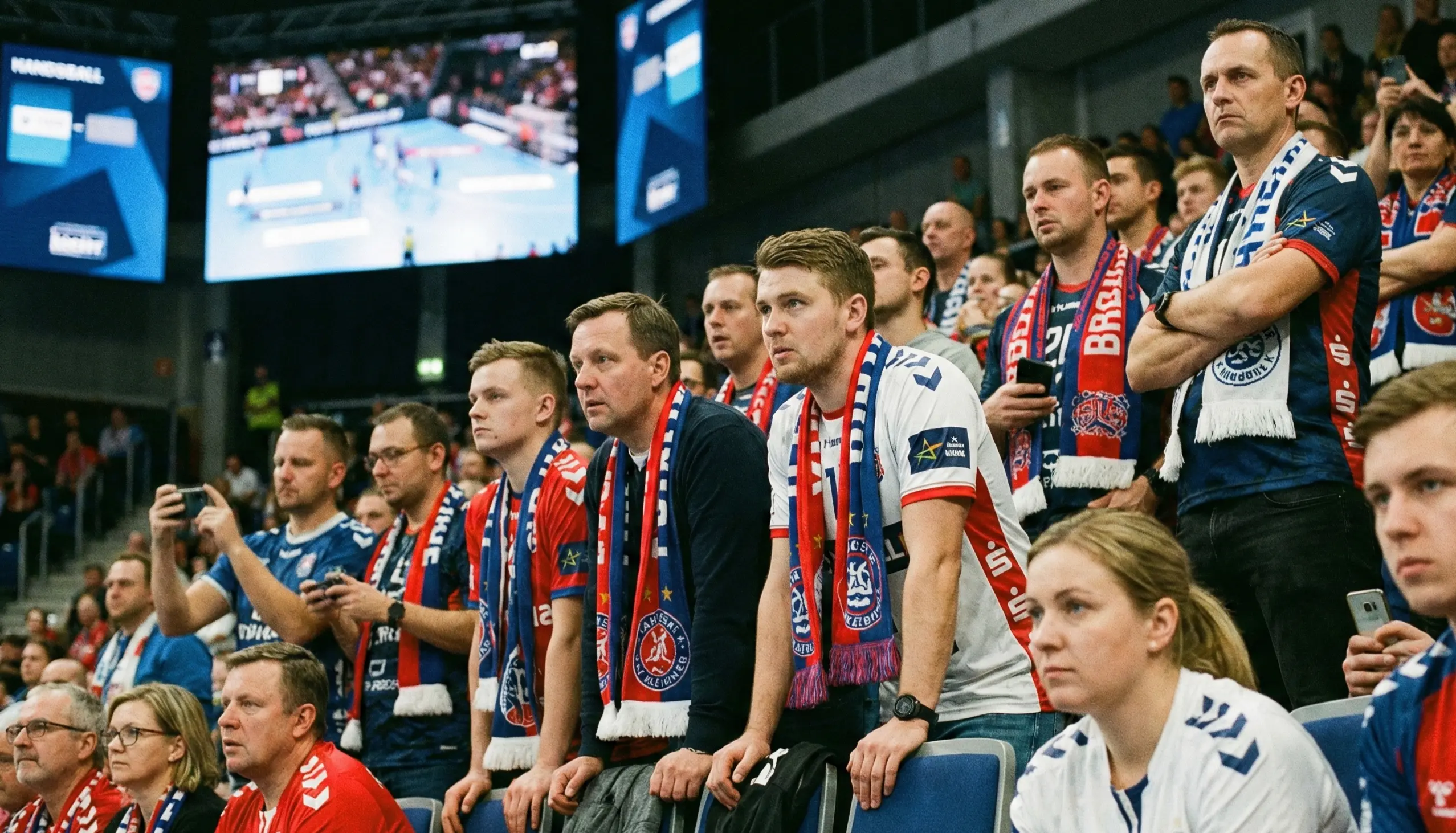 Handball-Fans in der Arena verfolgen ein Spiel auf Bildschirmen