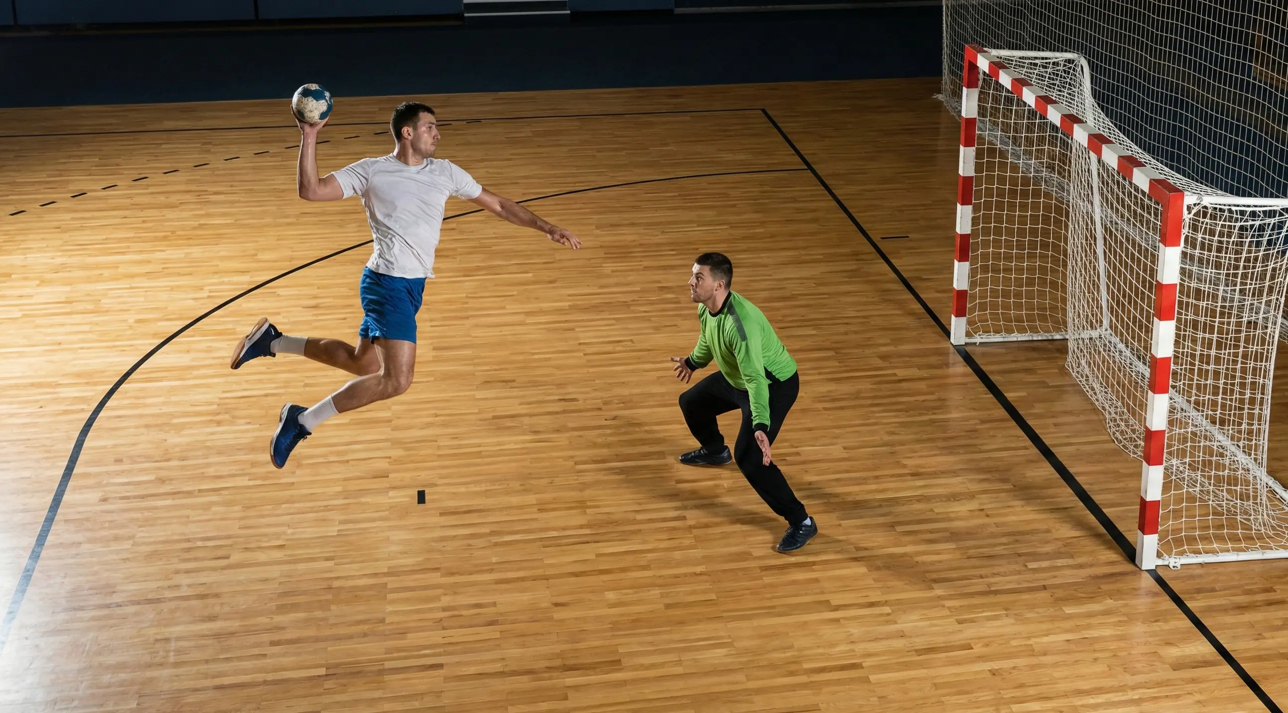 Handball-Spieler beim Torwurf mit Torhüter in Abwehrposition